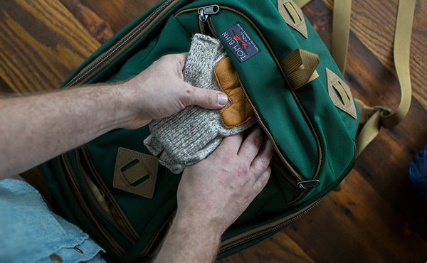 A person sliding a pair of winter gloves into the bottom pocket of the Guide's Edition Synik 22.